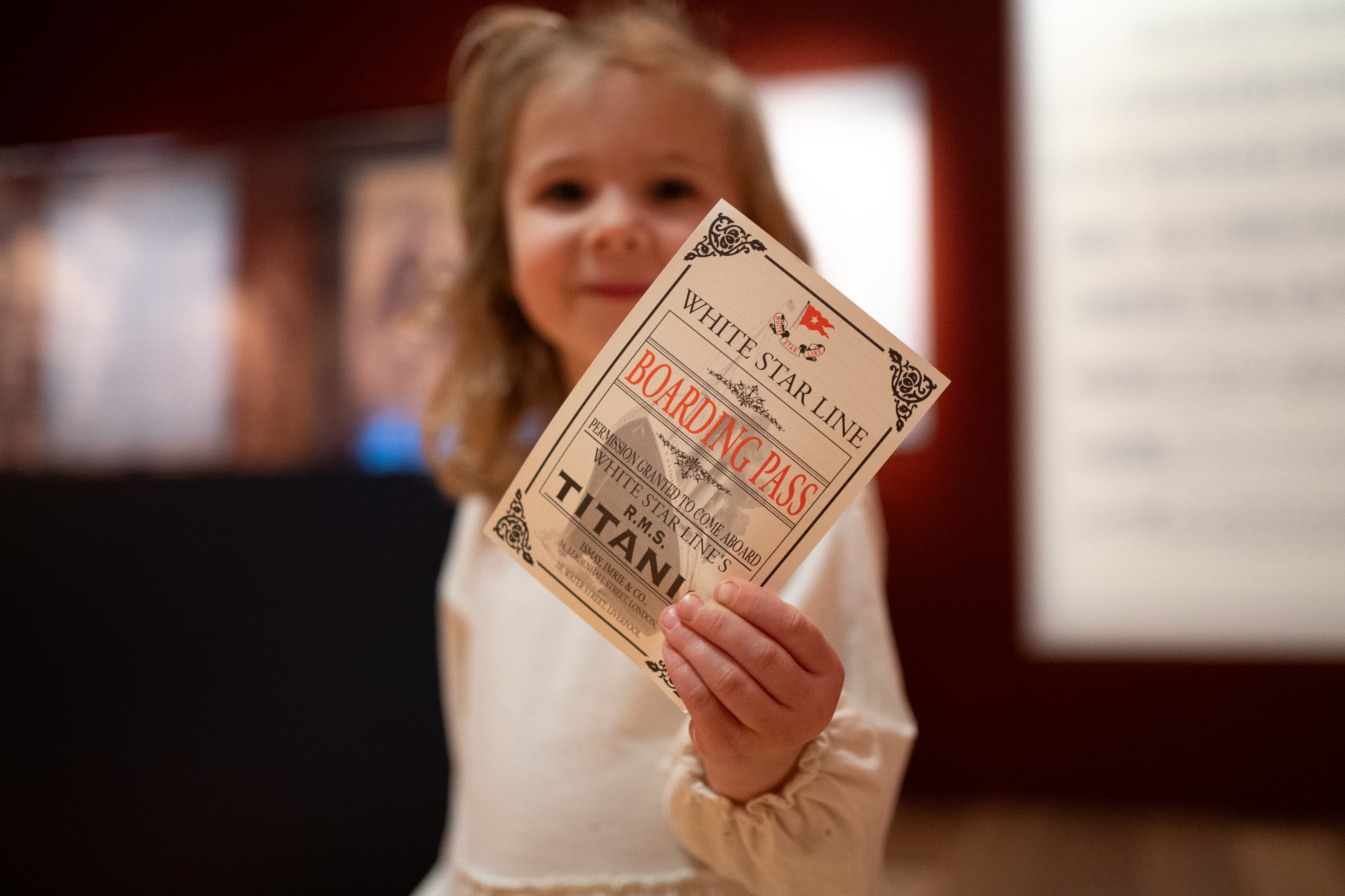 Image of a Young child holding up their replica boarding ticket for Titanic: The Artifact Exhibition
